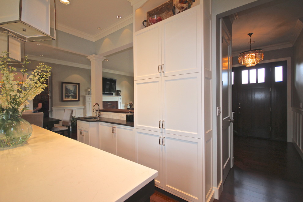 This is an example of a medium sized traditional u-shaped kitchen/diner in Seattle with an island, recessed-panel cabinets, white cabinets, engineered stone countertops, white splashback, metro tiled splashback, stainless steel appliances, a submerged sink and medium hardwood flooring.