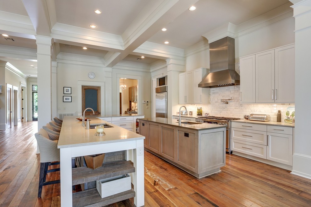 Inspiration for a transitional galley medium tone wood floor and brown floor eat-in kitchen remodel in New Orleans with an undermount sink, shaker cabinets, white cabinets, white backsplash, stainless steel appliances, two islands and gray countertops