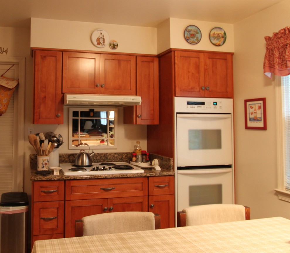 Klassisk inredning av ett kök, med en undermonterad diskho, luckor med infälld panel, skåp i mellenmörkt trä, granitbänkskiva, vitt stänkskydd, vita vitvaror och linoleumgolv