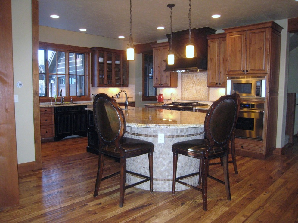 Example of a large classic medium tone wood floor eat-in kitchen design in Denver with an undermount sink, raised-panel cabinets, medium tone wood cabinets, granite countertops, beige backsplash, stone tile backsplash and stainless steel appliances