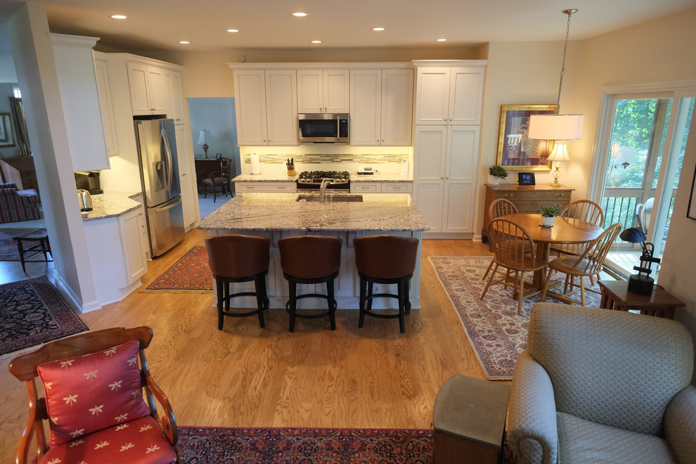 Inspiration for a large transitional l-shaped light wood floor open concept kitchen remodel in Atlanta with a double-bowl sink, flat-panel cabinets, white cabinets, granite countertops, multicolored backsplash, mosaic tile backsplash, stainless steel appliances and an island