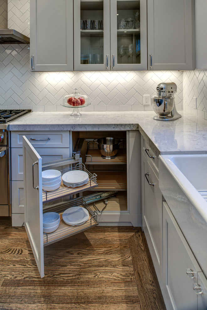 Inspiration for a mid-sized transitional l-shaped medium tone wood floor enclosed kitchen remodel in San Francisco with a farmhouse sink, raised-panel cabinets, gray cabinets, quartz countertops, white backsplash, porcelain backsplash, stainless steel appliances and an island