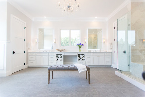 Spacious luxury bathroom with white double vanities, glass shower, chandelier, and central bench seating