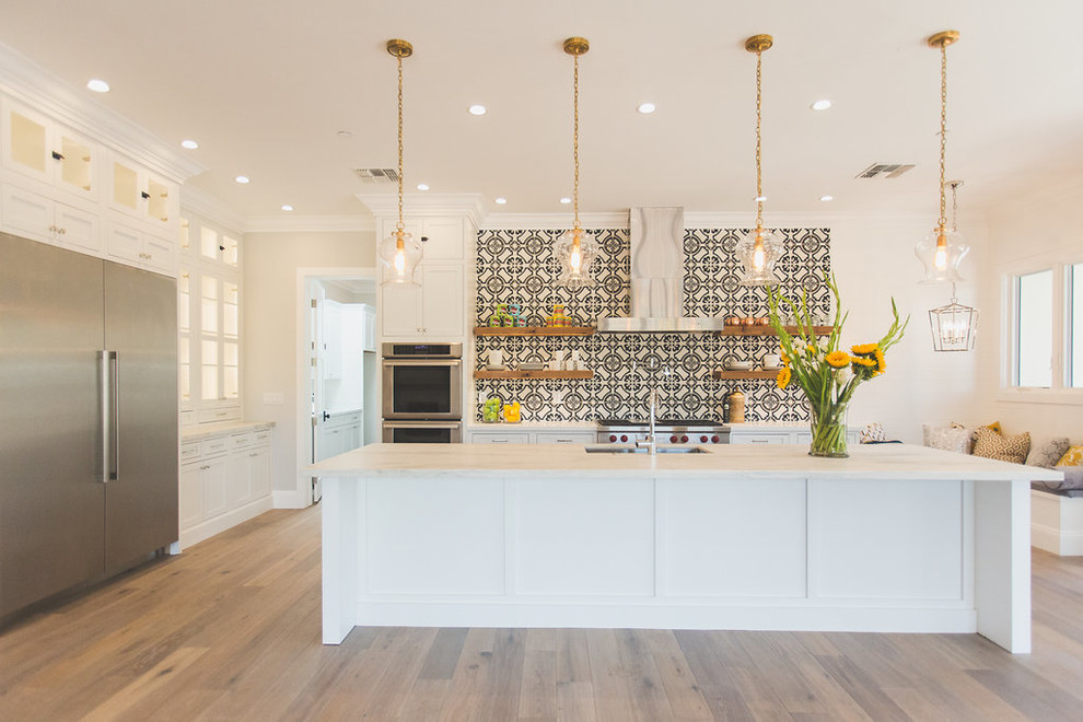 Large classic galley kitchen/diner in Phoenix with white cabinets, stainless steel appliances, an island, a double-bowl sink, recessed-panel cabinets, multi-coloured splashback, medium hardwood flooring, engineered stone countertops, cement tile splashback, brown floors and white worktops.