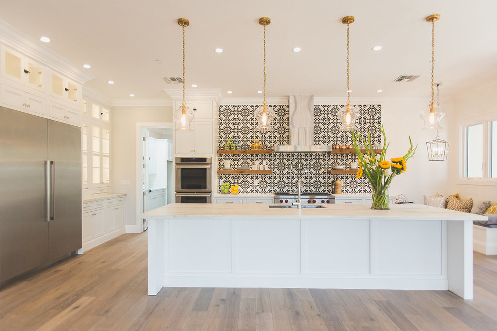 Example of a large transitional galley medium tone wood floor and brown floor eat-in kitchen design in Phoenix with white cabinets, stainless steel appliances, an island, a double-bowl sink, recessed-panel cabinets, multicolored backsplash, quartz countertops, cement tile backsplash and white countertops