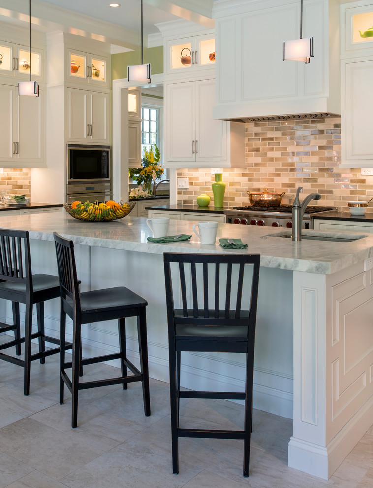 Klassisk inredning av ett kök, med luckor med infälld panel, vita skåp, flerfärgad stänkskydd, rostfria vitvaror och en köksö