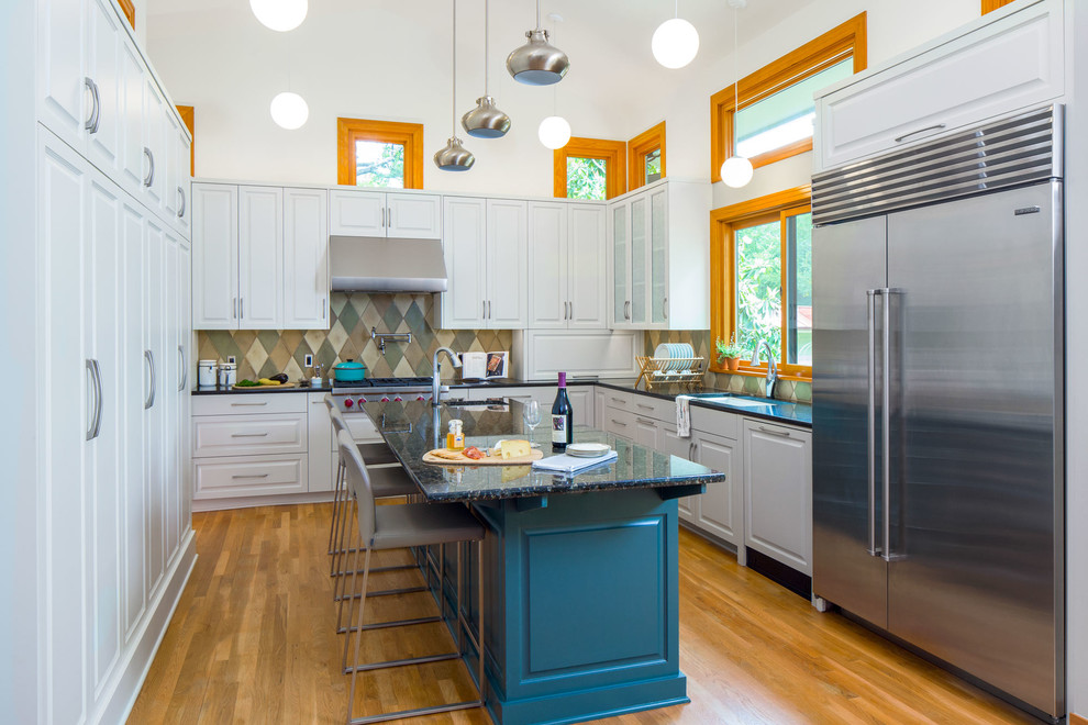 Example of a mid-sized transitional u-shaped medium tone wood floor enclosed kitchen design in Austin with an undermount sink, raised-panel cabinets, white cabinets, granite countertops, green backsplash, ceramic backsplash, stainless steel appliances and an island