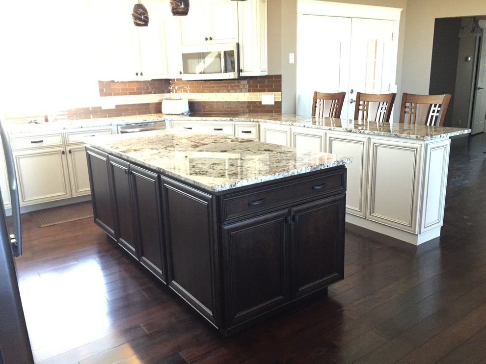Example of a large transitional u-shaped medium tone wood floor open concept kitchen design in Other with a double-bowl sink, raised-panel cabinets, yellow cabinets, granite countertops, brown backsplash, stainless steel appliances and two islands