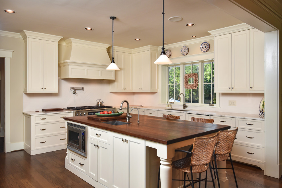 Bild på ett vintage l-kök, med en undermonterad diskho, marmorbänkskiva, vitt stänkskydd, rostfria vitvaror, mörkt trägolv, en köksö, brunt golv, skåp i shakerstil och beige skåp