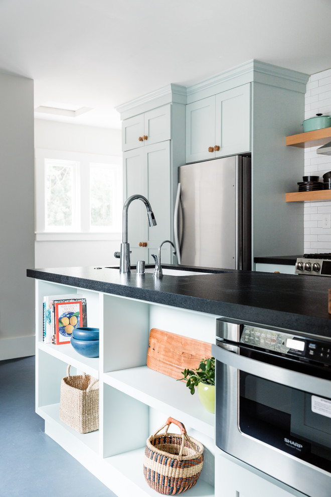Foto på ett mellanstort vintage svart kök, med en nedsänkt diskho, skåp i shakerstil, blå skåp, granitbänkskiva, vitt stänkskydd, stänkskydd i tegel, rostfria vitvaror, linoleumgolv, en halv köksö och blått golv