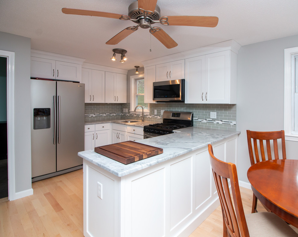Example of a mid-sized transitional u-shaped light wood floor and brown floor eat-in kitchen design in Boston with a single-bowl sink, flat-panel cabinets, white cabinets, granite countertops, gray backsplash, subway tile backsplash, stainless steel appliances, a peninsula and white countertops