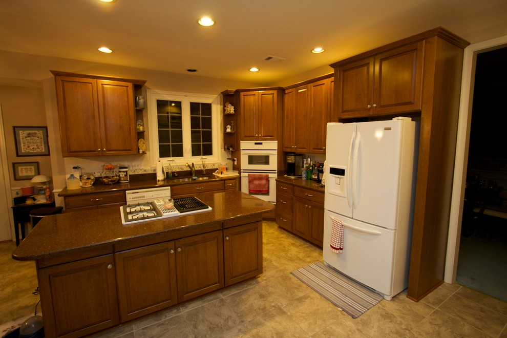 Example of a farmhouse l-shaped kitchen design in Baltimore with a double-bowl sink, raised-panel cabinets, medium tone wood cabinets, white appliances and an island