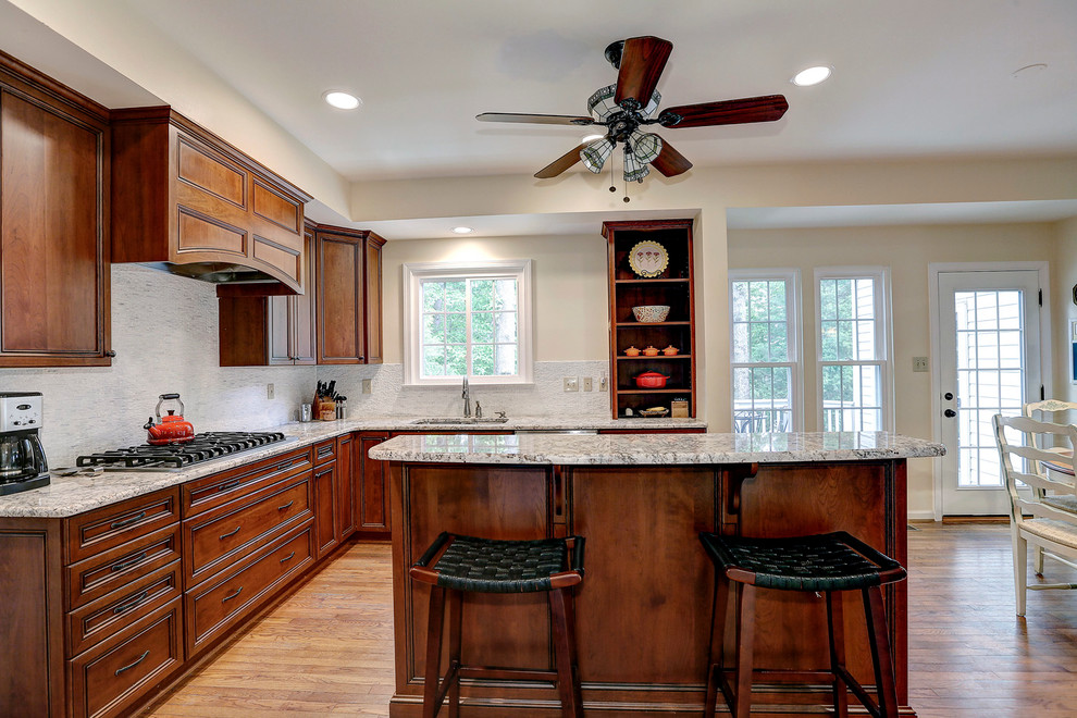 This is an example of a traditional l-shaped open plan kitchen in Baltimore with a double-bowl sink, recessed-panel cabinets, medium wood cabinets, granite worktops, white splashback, stainless steel appliances, medium hardwood flooring and an island.