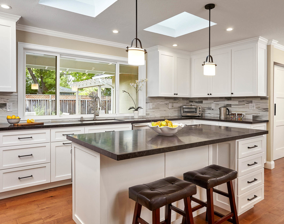 Example of a large transitional u-shaped medium tone wood floor and brown floor eat-in kitchen design in San Francisco with shaker cabinets, white cabinets, granite countertops, multicolored backsplash, stainless steel appliances, an island, black countertops, an undermount sink and marble backsplash