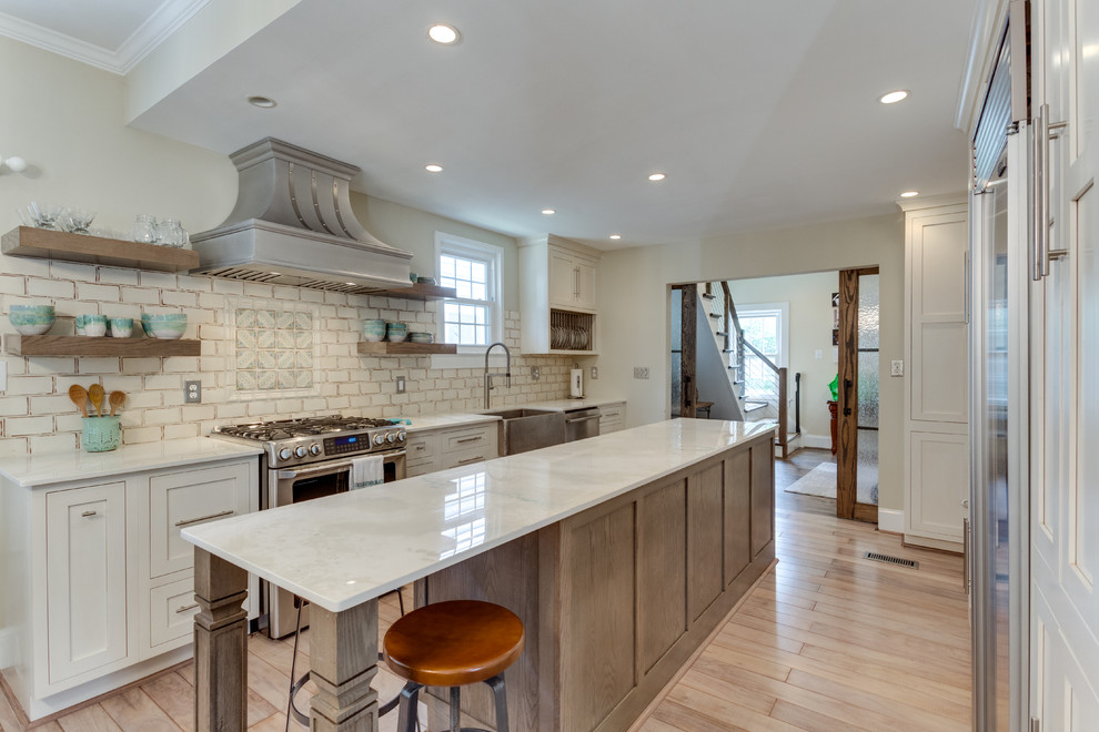 This is an example of a medium sized farmhouse galley kitchen in DC Metro with a belfast sink, laminate countertops, stainless steel appliances, light hardwood flooring and an island.
