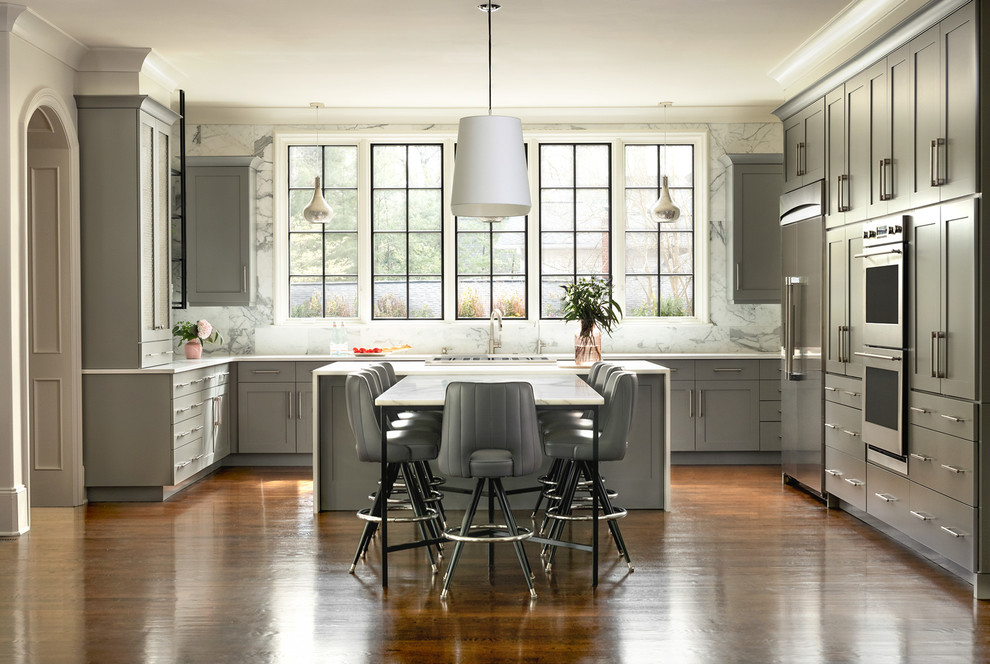 Inspiration for a classic l-shaped kitchen/diner in Charlotte with shaker cabinets, grey cabinets, white splashback, stone slab splashback, stainless steel appliances, medium hardwood flooring, an island, brown floors and white worktops.