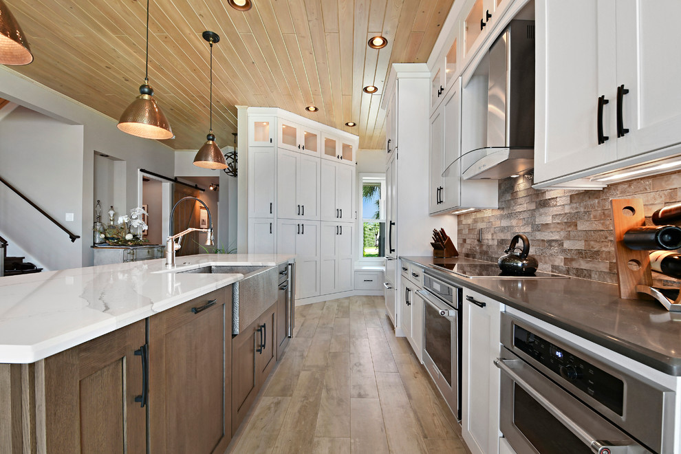 Inspiration for a large transitional l-shaped light wood floor and beige floor eat-in kitchen remodel in Orlando with a farmhouse sink, shaker cabinets, white cabinets, marble countertops, beige backsplash, subway tile backsplash, stainless steel appliances and an island