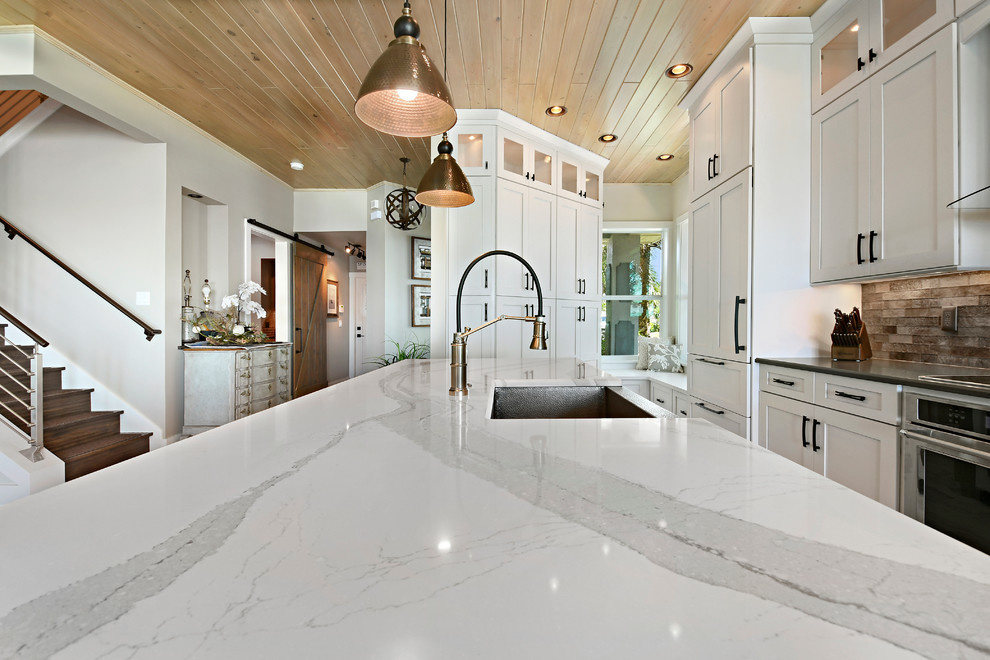 Large transitional l-shaped light wood floor and beige floor eat-in kitchen photo in Orlando with a farmhouse sink, shaker cabinets, white cabinets, marble countertops, beige backsplash, subway tile backsplash, stainless steel appliances and an island
