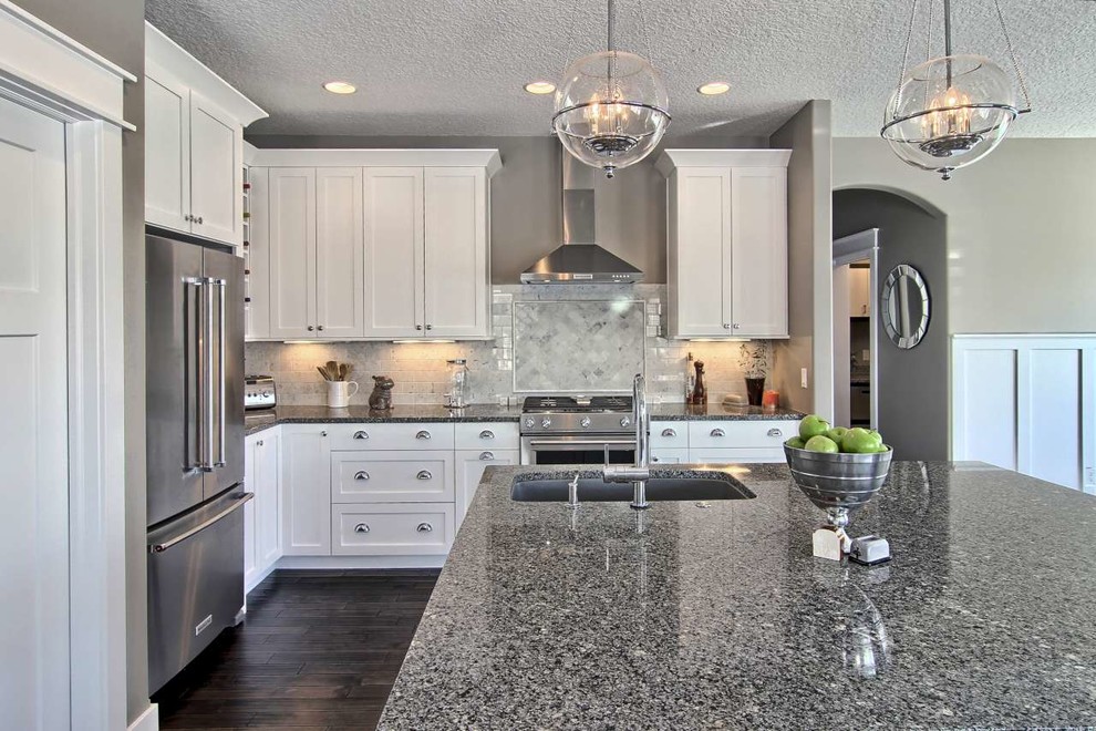 Open concept kitchen - mid-sized transitional l-shaped dark wood floor open concept kitchen idea in Other with a single-bowl sink, shaker cabinets, white cabinets, granite countertops, gray backsplash, stone tile backsplash, stainless steel appliances and an island