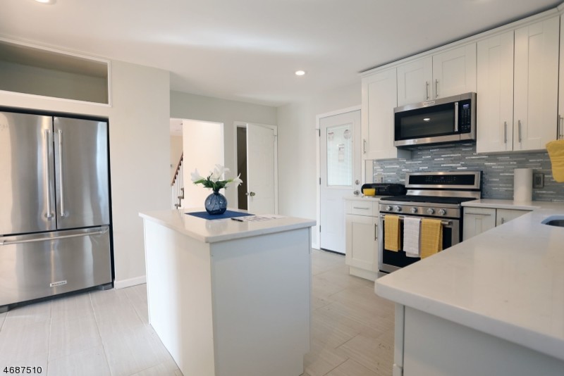 This is an example of a medium sized classic l-shaped enclosed kitchen in New York with a single-bowl sink, shaker cabinets, white cabinets, engineered stone countertops, grey splashback, stainless steel appliances, an island, grey floors, matchstick tiled splashback and porcelain flooring.
