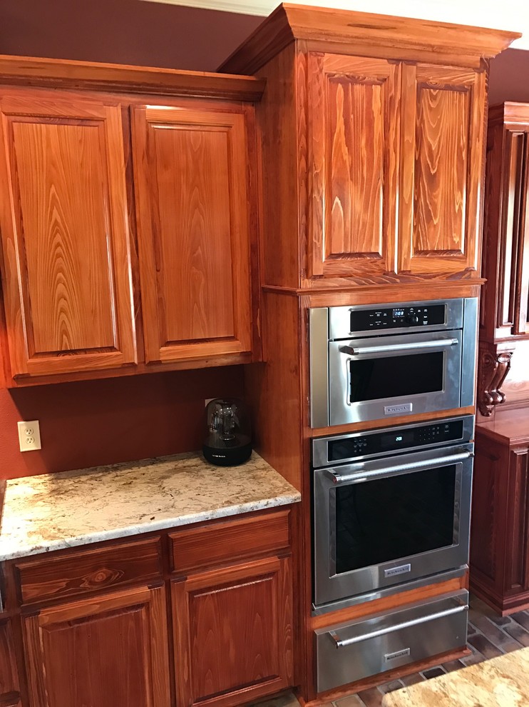 Exempel på ett avskilt klassiskt kök, med luckor med upphöjd panel, bruna skåp, granitbänkskiva, rostfria vitvaror, tegelgolv och en halv köksö