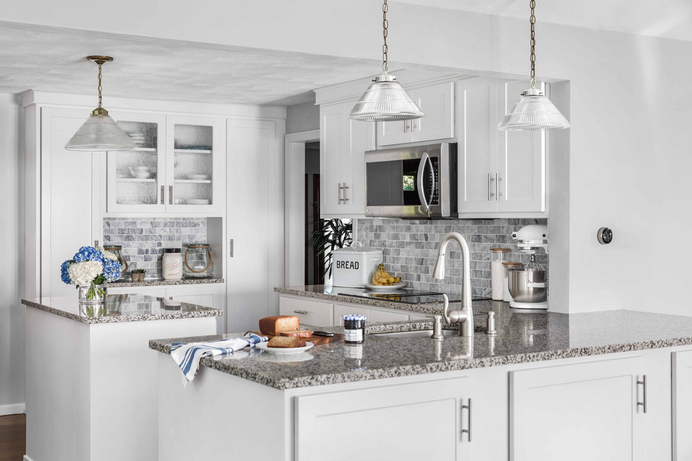 Bild på ett mycket stort funkis grå grått u-kök, med en enkel diskho, luckor med infälld panel, vita skåp, granitbänkskiva, grått stänkskydd, stänkskydd i marmor, rostfria vitvaror, mellanmörkt trägolv, en köksö och brunt golv