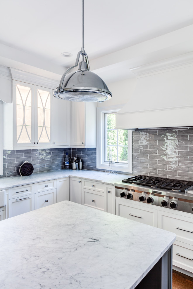 Example of a mid-sized transitional u-shaped light wood floor and brown floor open concept kitchen design in New York with a farmhouse sink, shaker cabinets, white cabinets, quartz countertops, gray backsplash, glass tile backsplash, paneled appliances and an island