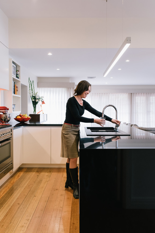 Design ideas for a medium sized contemporary u-shaped open plan kitchen in Melbourne with a double-bowl sink, flat-panel cabinets, white cabinets, granite worktops, red splashback, glass sheet splashback, stainless steel appliances, medium hardwood flooring and no island.