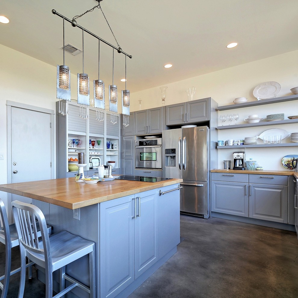 Example of a classic u-shaped concrete floor and gray floor kitchen design in Austin with raised-panel cabinets, blue cabinets, wood countertops, stainless steel appliances, an island and beige countertops