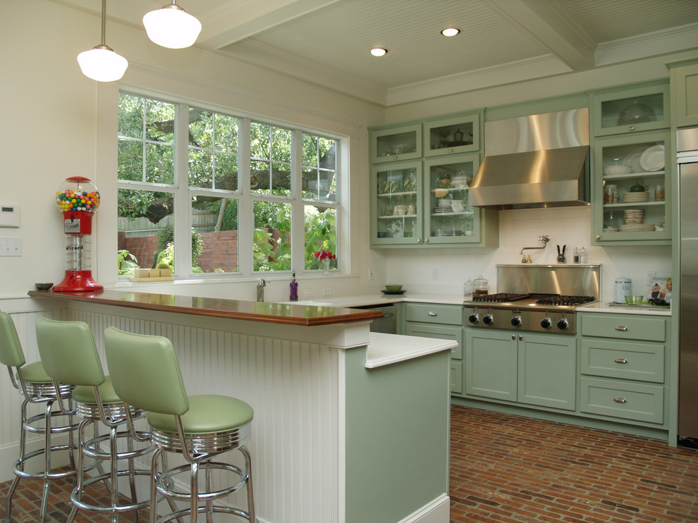 オースティンにあるトラディショナルスタイルのおしゃれなコの字型キッチン (ガラス扉のキャビネット、緑のキャビネット、白いキッチンパネル、シルバーの調理設備、サブウェイタイルのキッチンパネル、ステンレスのキッチンパネル) の写真