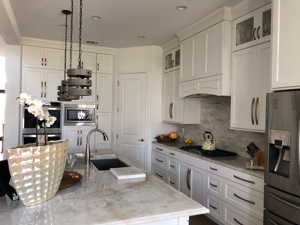 Photo of a large modern single-wall kitchen/diner in Austin with a single-bowl sink, shaker cabinets, white cabinets, quartz worktops, travertine splashback, stainless steel appliances, an island and brown floors.