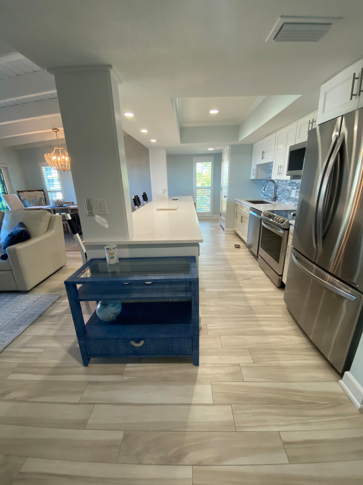 Open concept kitchen - large coastal galley porcelain tile and beige floor open concept kitchen idea in Tampa with an undermount sink, shaker cabinets, white cabinets, quartz countertops, blue backsplash, glass tile backsplash, stainless steel appliances, an island and white countertops
