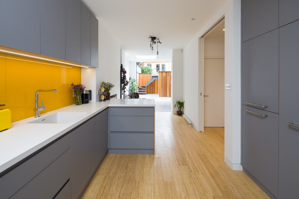 Modern inredning av ett mellanstort kök, med en undermonterad diskho, släta luckor, grå skåp, bänkskiva i koppar, gult stänkskydd, glaspanel som stänkskydd, integrerade vitvaror, bambugolv och brunt golv