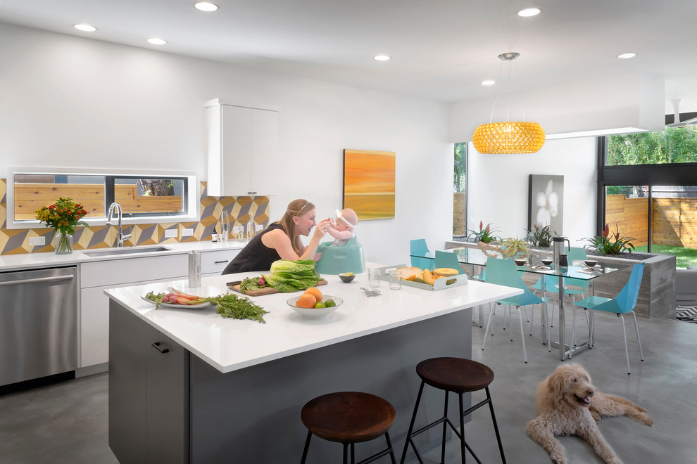 Photo of a medium sized modern l-shaped kitchen/diner in Austin with a submerged sink, flat-panel cabinets, white cabinets, engineered stone countertops, multi-coloured splashback, cement tile splashback, stainless steel appliances, concrete flooring and an island.