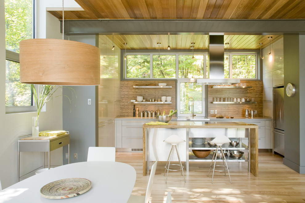 Ejemplo de cocina contemporánea abierta con armarios con paneles lisos, puertas de armario grises, salpicadero marrón, electrodomésticos de acero inoxidable y suelo de madera clara