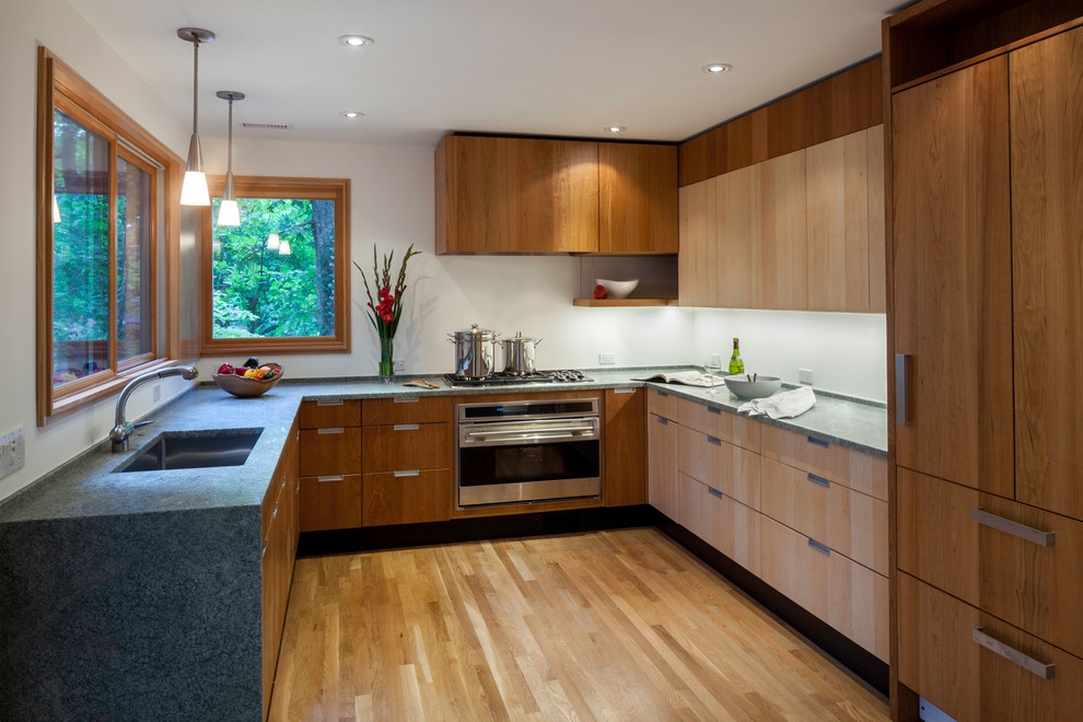 На фото: п-образная кухня в современном стиле с врезной мойкой, плоскими фасадами, фасадами цвета дерева среднего тона и техникой под мебельный фасад