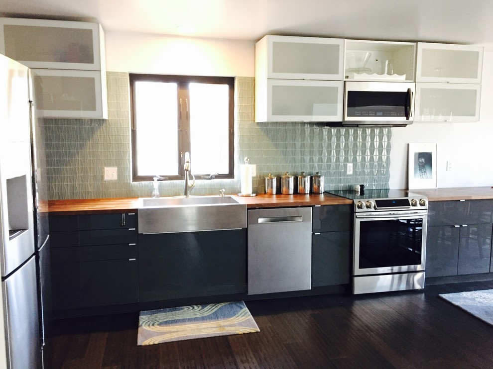 This is an example of a contemporary l-shaped kitchen/diner in Kansas City with a belfast sink, flat-panel cabinets, grey cabinets, wood worktops, grey splashback, glass tiled splashback, stainless steel appliances, dark hardwood flooring and no island.