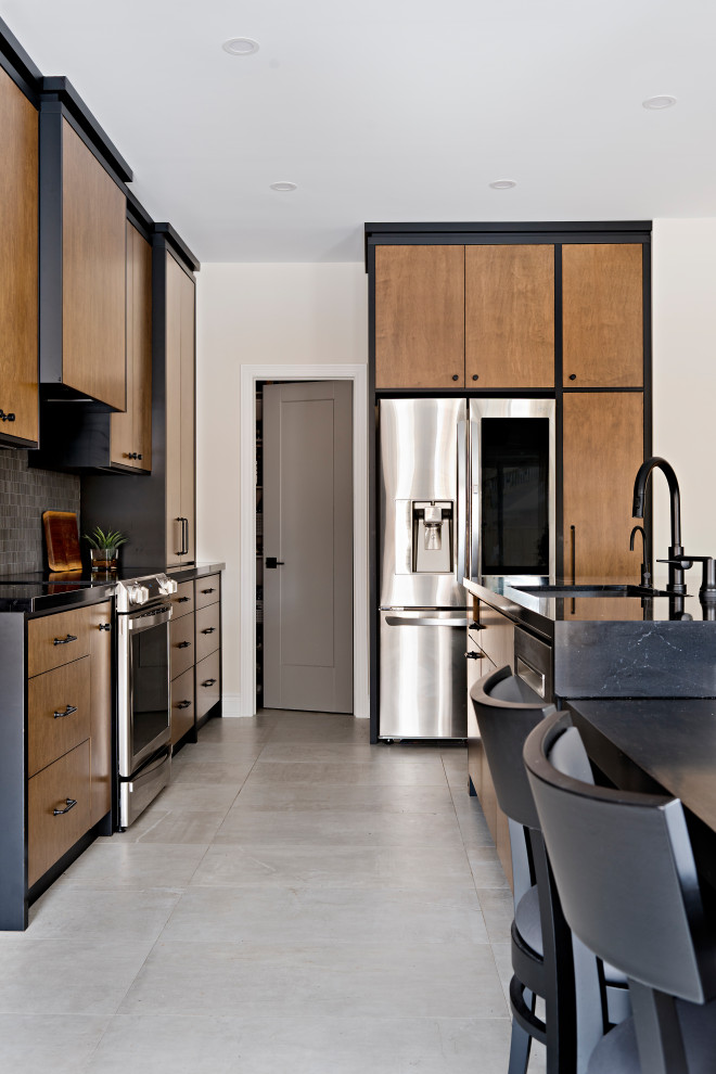 Photo of a large eclectic l-shaped open plan kitchen in Toronto with a submerged sink, flat-panel cabinets, medium wood cabinets, engineered stone countertops, black splashback, porcelain splashback, stainless steel appliances, porcelain flooring, an island, grey floors and black worktops.