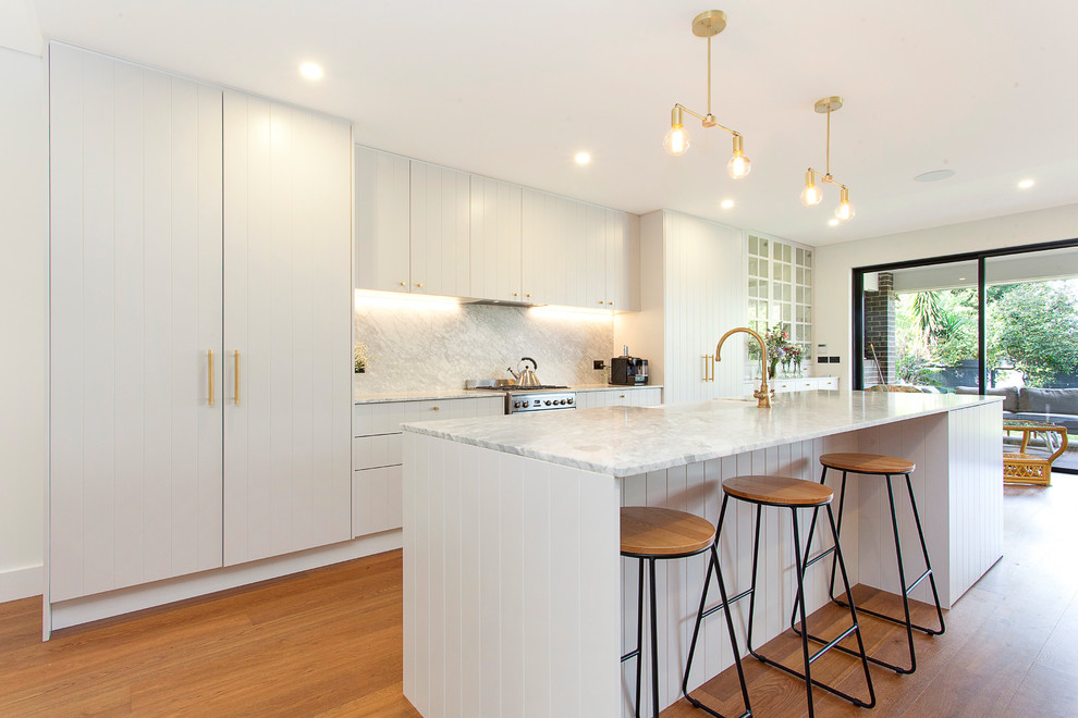 Kitchen - contemporary galley medium tone wood floor and brown floor kitchen idea in Sydney with a farmhouse sink, flat-panel cabinets, white cabinets, white backsplash, stone slab backsplash, stainless steel appliances, an island and white countertops