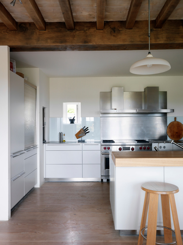 Foto de cocina de estilo de casa de campo con armarios con paneles lisos, puertas de armario blancas, electrodomésticos de acero inoxidable, suelo de madera en tonos medios y una isla