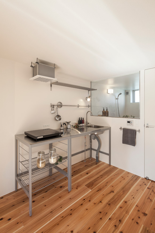 Bild på ett litet funkis kök, med en enkel diskho, bänkskiva i rostfritt stål och mellanmörkt trägolv