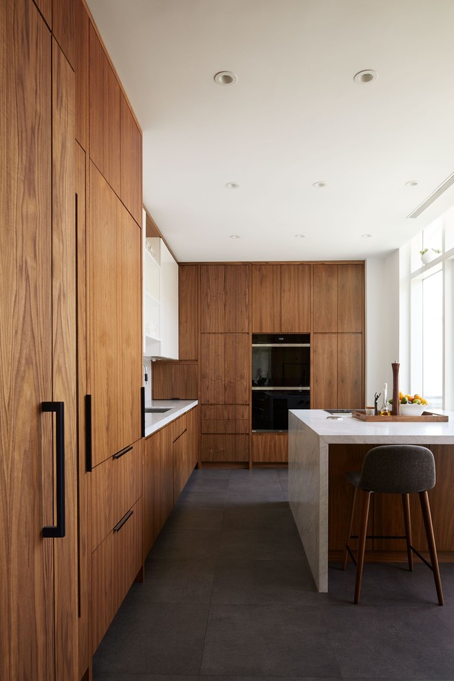 Modelo de cocina contemporánea con armarios con paneles lisos, puertas de armario de madera oscura, electrodomésticos negros, una isla, suelo gris y encimeras blancas