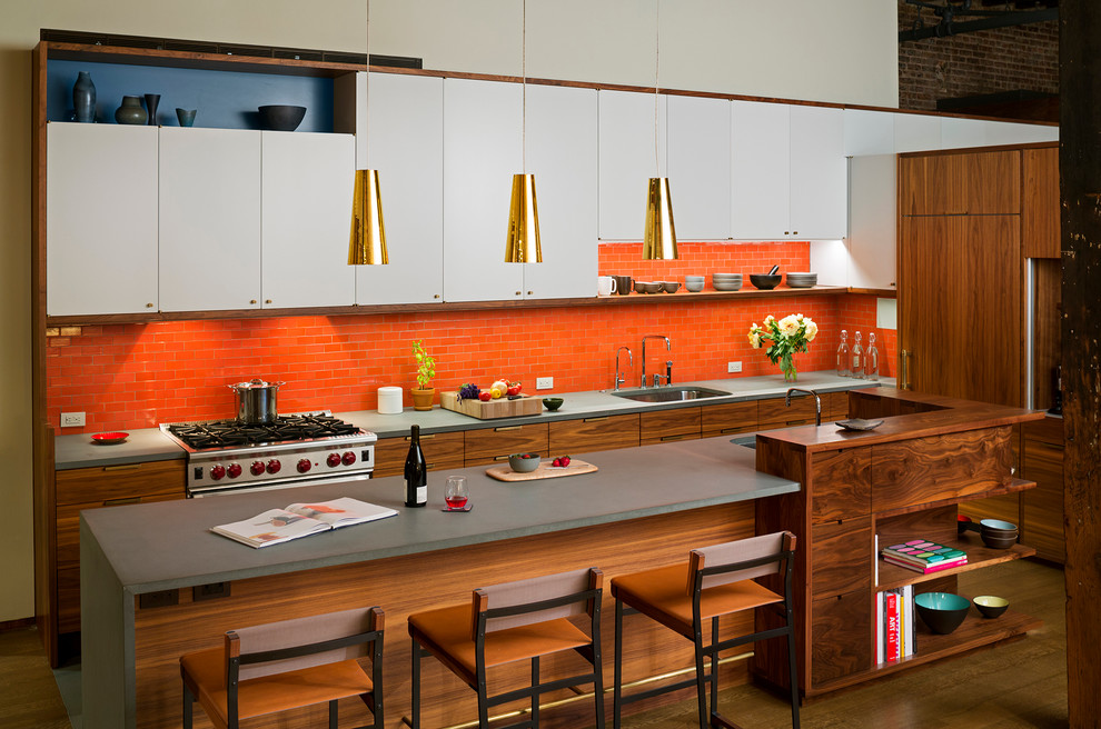 Moderne Küche mit flächenbündigen Schrankfronten, weißen Schränken, Mineralwerkstoff-Arbeitsplatte, Rückwand aus Keramikfliesen, Elektrogeräten mit Frontblende, Kücheninsel, Unterbauwaschbecken, Küchenrückwand in Orange und dunklem Holzboden in New York