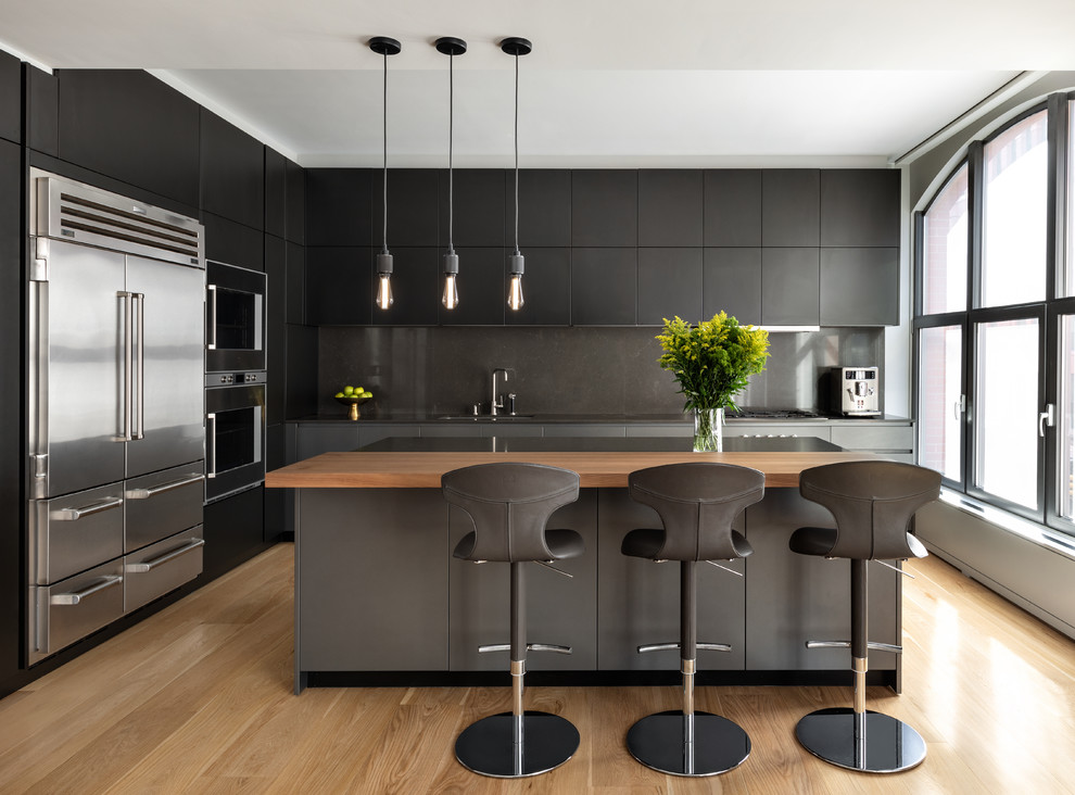 Photo of a large contemporary l-shaped open plan kitchen in New York with a submerged sink, flat-panel cabinets, grey cabinets, marble worktops, grey splashback, marble splashback, stainless steel appliances, light hardwood flooring, an island, beige floors and grey worktops.