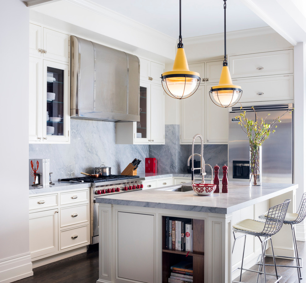 Klassisk inredning av ett grå grått l-kök, med en undermonterad diskho, luckor med infälld panel, vita skåp, grått stänkskydd, stänkskydd i sten, rostfria vitvaror, mörkt trägolv, en köksö och brunt golv