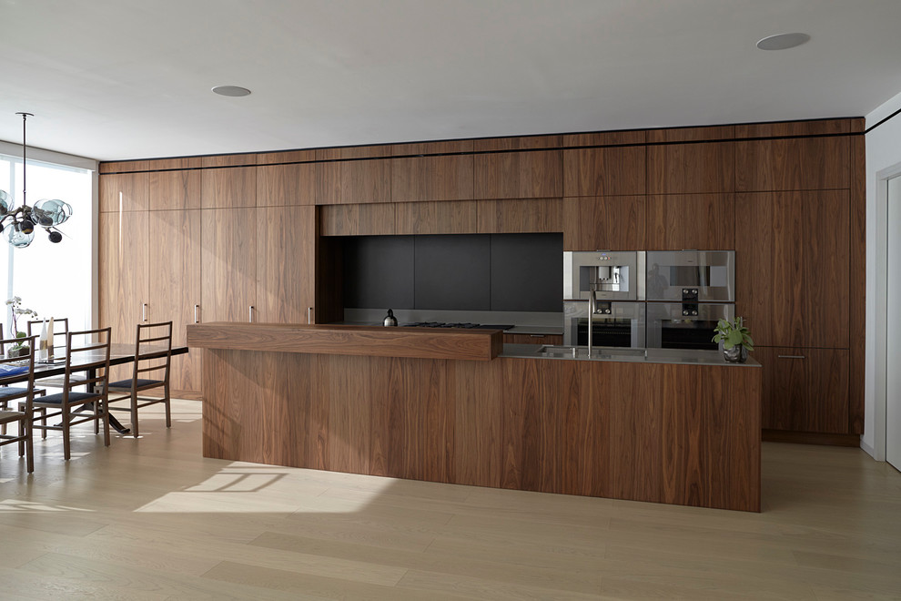Example of a large trendy galley light wood floor eat-in kitchen design in New York with an undermount sink, flat-panel cabinets, dark wood cabinets, solid surface countertops, black backsplash, stainless steel appliances and an island