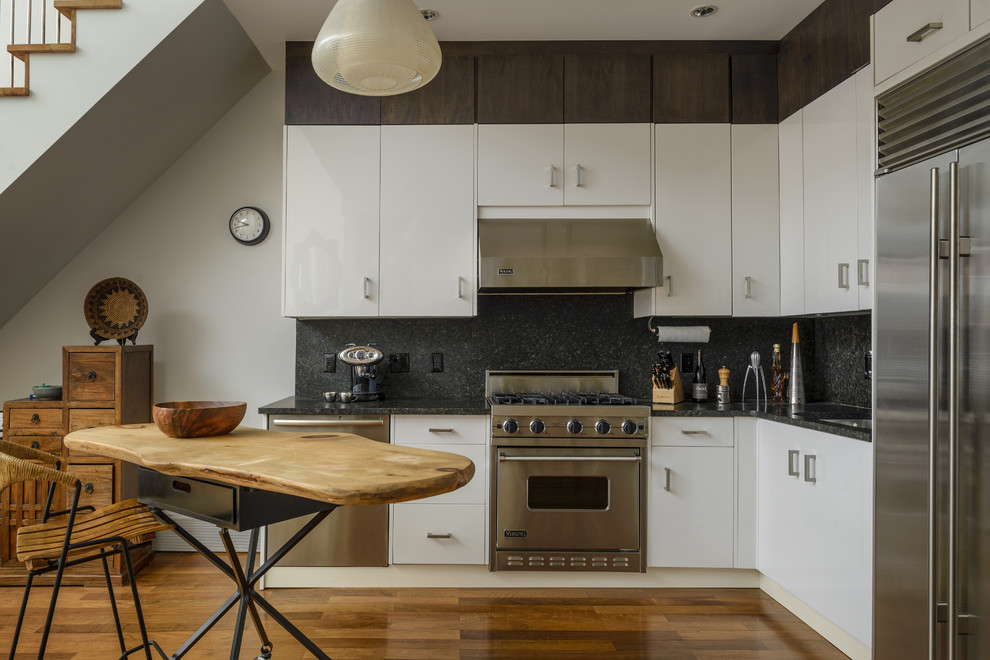 Exempel på ett mellanstort klassiskt svart svart l-kök, med en undermonterad diskho, släta luckor, vita skåp, svart stänkskydd, stänkskydd i sten, rostfria vitvaror, mellanmörkt trägolv, en köksö och brunt golv