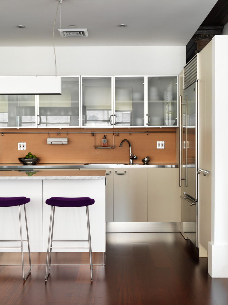 Example of a mid-sized trendy kitchen design in New York with glass-front cabinets, stainless steel countertops, brown backsplash and an island