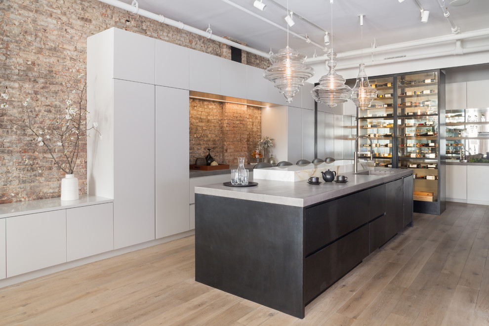 Large contemporary l-shaped open plan kitchen in New York with a submerged sink, flat-panel cabinets, concrete worktops, light hardwood flooring, an island, white cabinets, red splashback, brick splashback and beige floors.