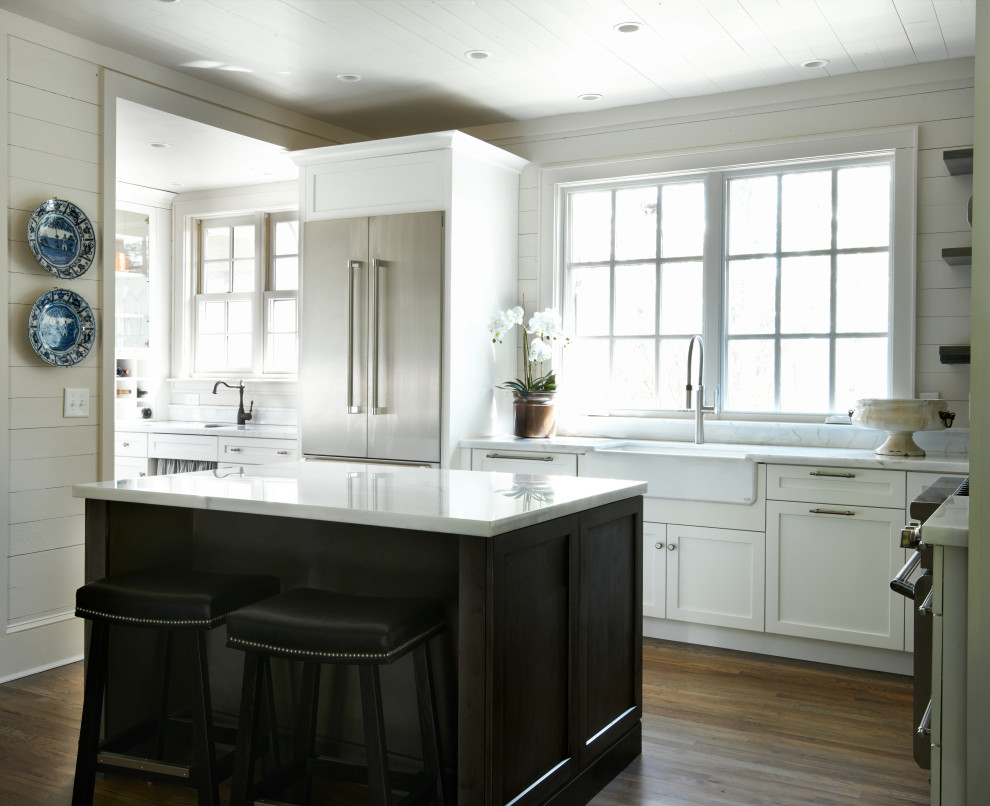 Klassisk inredning av ett mellanstort vit linjärt vitt kök och matrum, med en dubbel diskho, luckor med infälld panel, vita skåp, granitbänkskiva, vitt stänkskydd, rostfria vitvaror, mellanmörkt trägolv, en köksö och brunt golv